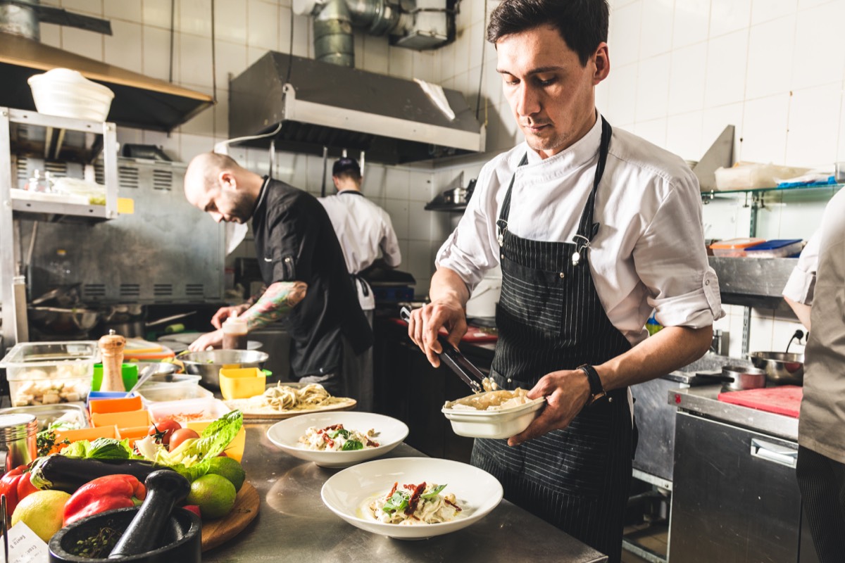 Professional chef cooking in the kitchen restaurant at the hotel, preparing dinner. A cook in an apron makes a salad of vegetables and pizza.